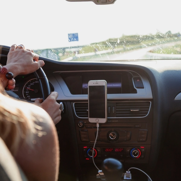 A female driving a car down the freeway with her iphone plugged into the console. 