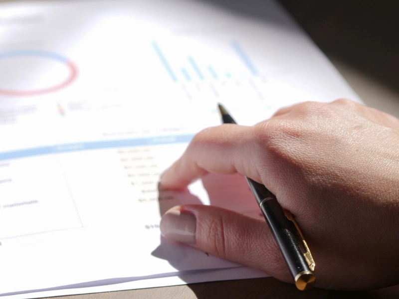A close-up view of a hand holding a pen and examining tax planning on investment gains.
