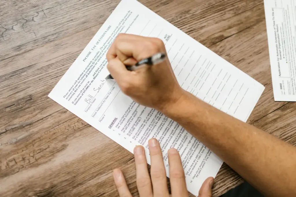 Close-up of a hand holding a pen over income tax questionnaire on a wooden table. Image complements the blog titled Multi State Tax Filing.