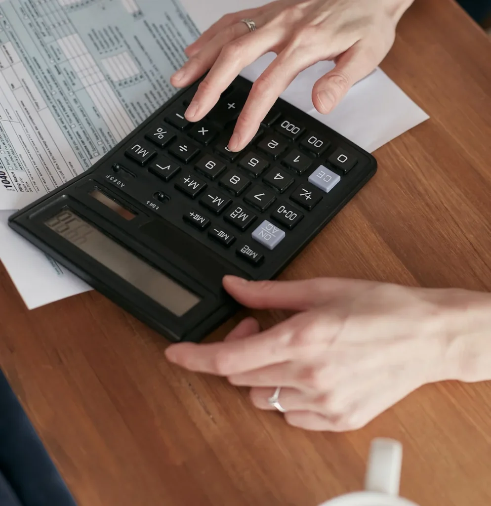 Person calculating finances with a calculator and document on a wooden desk. Image complements the blog, Multi State Tax Filing.